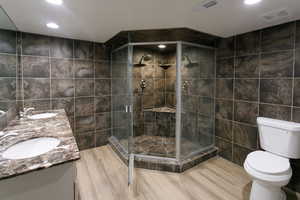 Bathroom featuring tile walls, a stall shower, double vanity, recessed lighting, and light wood-style floors