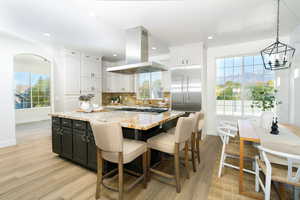 Kitchen with light stone countertops, dark cabinets, island range hood, light wood-type flooring, and a kitchen island