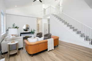 Living area with high vaulted ceiling, stairway, light wood-style flooring, ceiling fan, and recessed lighting