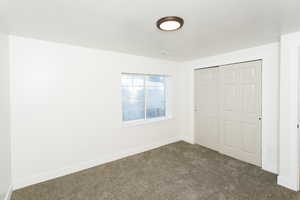 Unfurnished bedroom with dark colored carpet, a closet, and a textured ceiling