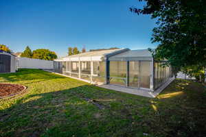Back of house featuring a sunroom, an exterior structure, a storage unit, a fenced backyard, and a lanai