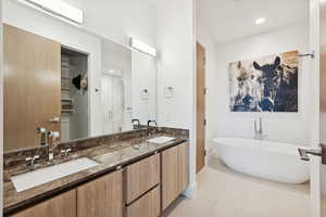 Primary bath en suite featuring light tile, separate shower, double vanity, a soaking tub, and recessed lighting.