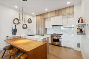 Kitchen with breakfast peninsula, 6 burner Wolf range, light grain hardwood floors, open shelves, and modern cabinets.