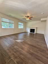 Unfurnished living room featuring a textured ceiling, dark wood-type flooring, a fireplace, and a ceiling fan