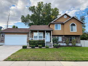 Split level home with stone siding, covered porch, stucco siding, driveway, and an attached garage