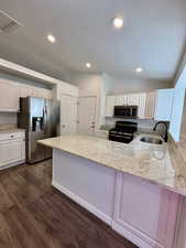 Kitchen with vaulted ceiling, light stone countertops, a textured ceiling, white cabinetry, and stainless steel appliances