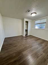 Unfurnished bedroom featuring dark wood finished floors, a closet, and a textured ceiling