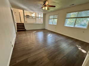 Unfurnished living room with dark wood-style floors, ceiling fan, stairway, and a textured ceiling