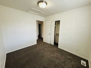 Unfurnished bedroom featuring dark colored carpet, attic access, a closet, and a textured ceiling