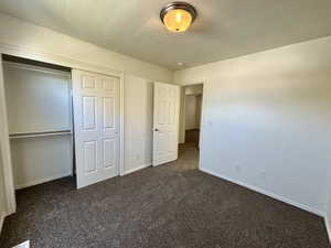 Unfurnished bedroom with a textured ceiling, dark colored carpet, and a closet