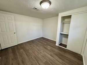 Unfurnished bedroom with a textured ceiling, dark wood-style floors, and a closet