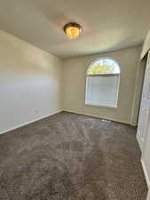 Empty room with a textured ceiling and dark colored carpet