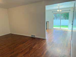Living room and kitchen pictured with dark wood-style flooring and a chandelier
