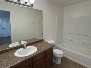 Primary bedroom bathroom with a textured ceiling, vanity, shower / washtub combination, and dark tile patterned floors