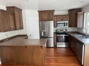Kitchen featuring appliances with stainless steel finishes, a peninsula, a breakfast bar area, dark wood finished floors, and a textured ceiling