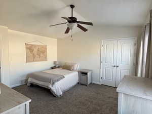 Main primary bedroom w/ vaulted ceiling, dark colored carpet, a closet, and ceiling fan
