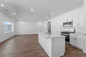 Kitchen with stainless steel appliances, white cabinetry, an island with sink, dark wood-style flooring, and recessed lighting