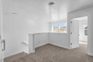 Hallway featuring light colored carpet, an upstairs landing, and a textured ceiling