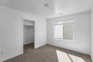 Unfurnished bedroom with carpet, a walk in closet, and a textured ceiling