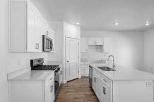Kitchen featuring stainless steel appliances, dark wood-style flooring, white cabinets, light stone countertops, and an island with sink