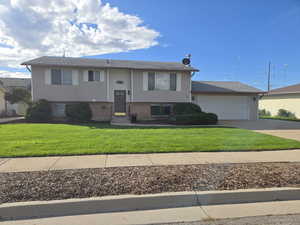Split foyer home featuring concrete driveway, a front lawn, brick siding, and an attached garage