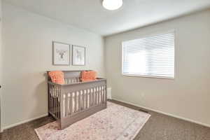 Carpeted bedroom featuring a nursery area and baseboards