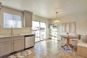 Kitchen with gray cabinets, stainless steel dishwasher, light tile patterned floors, decorative light fixtures, and a textured ceiling
