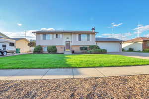 Raised ranch with brick siding, a front lawn, an attached garage, and driveway