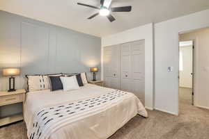 Carpeted bedroom featuring a closet, ceiling fan, and a decorative wall