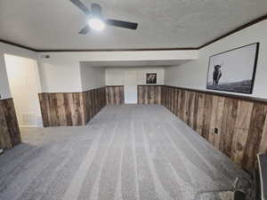 Finished below grade area featuring wooden walls, wainscoting, ornamental molding, a textured ceiling, and carpet flooring