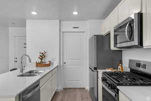 Kitchen with appliances with stainless steel finishes, a peninsula, white cabinets, light stone counters, and recessed lighting