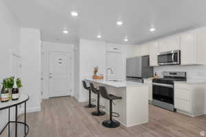 Kitchen featuring a peninsula, a breakfast bar, stainless steel appliances, light wood-style flooring, and recessed lighting
