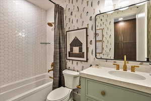 Bathroom featuring wallpapered walls, shower / bath combination with curtain, and vanity