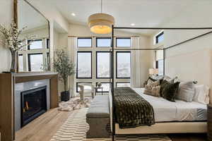 Bedroom with wood finished floors, a glass covered fireplace, recessed lighting, and high vaulted ceiling