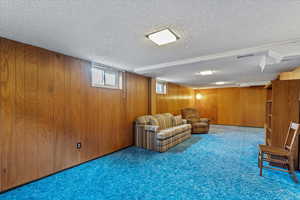 Carpeted living room featuring wooden walls and a textured ceiling