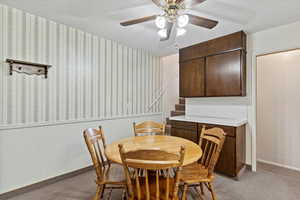 Dining area with dark colored carpet, wallpapered walls, a ceiling fan, and wainscoting