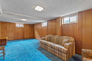 Carpeted living room featuring a textured ceiling and wooden walls