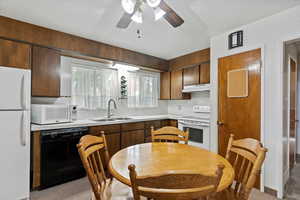 Kitchen with white appliances, light countertops, under cabinet range hood, light carpet, and a ceiling fan