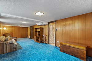 Carpeted living room featuring wooden walls and a textured ceiling