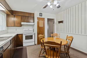 Kitchen with white electric range, light countertops, wallpapered walls, dark colored carpet, and under cabinet range hood