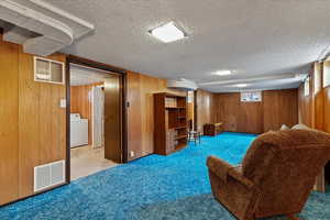 Sitting room with wooden walls, carpet, washer / clothes dryer, and a textured ceiling
