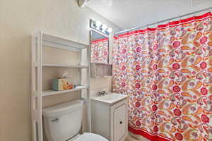 Bathroom with vanity, a textured wall, a shower with curtain, and a textured ceiling