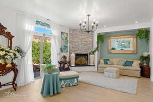 Living room with wood finished floors, a stone fireplace, and a chandelier