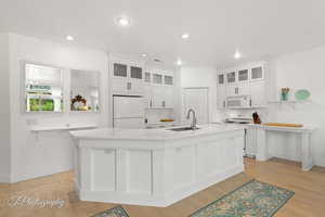 Kitchen with white appliances, white cabinets, glass insert cabinets, recessed lighting, and a spacious island