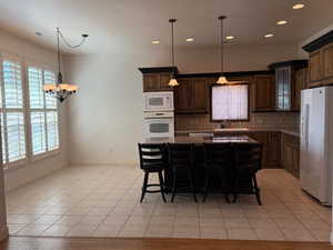Kitchen featuring a breakfast bar area, pendant lighting, white appliances, backsplash, and a center island