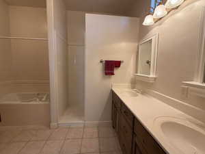 Bathroom with light tile patterned floors, double vanity, a shower stall, and a garden tub