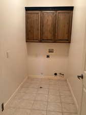 Laundry area with gas dryer hookup, hookup for a washing machine, light tile patterned floors, cabinet space, and hookup for an electric dryer