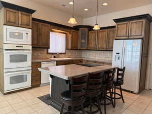 Kitchen featuring white appliances, a kitchen bar, light tile patterned flooring, a center island, and decorative light fixtures