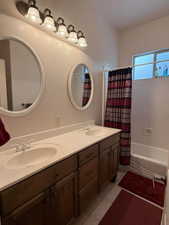 Bathroom with light tile patterned floors, shower / bath combo with shower curtain, and double vanity