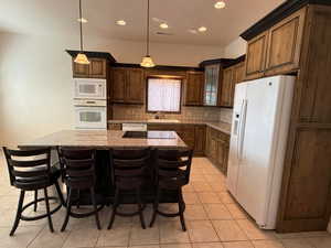 Kitchen featuring a kitchen breakfast bar, decorative light fixtures, white appliances, backsplash, and light tile patterned flooring